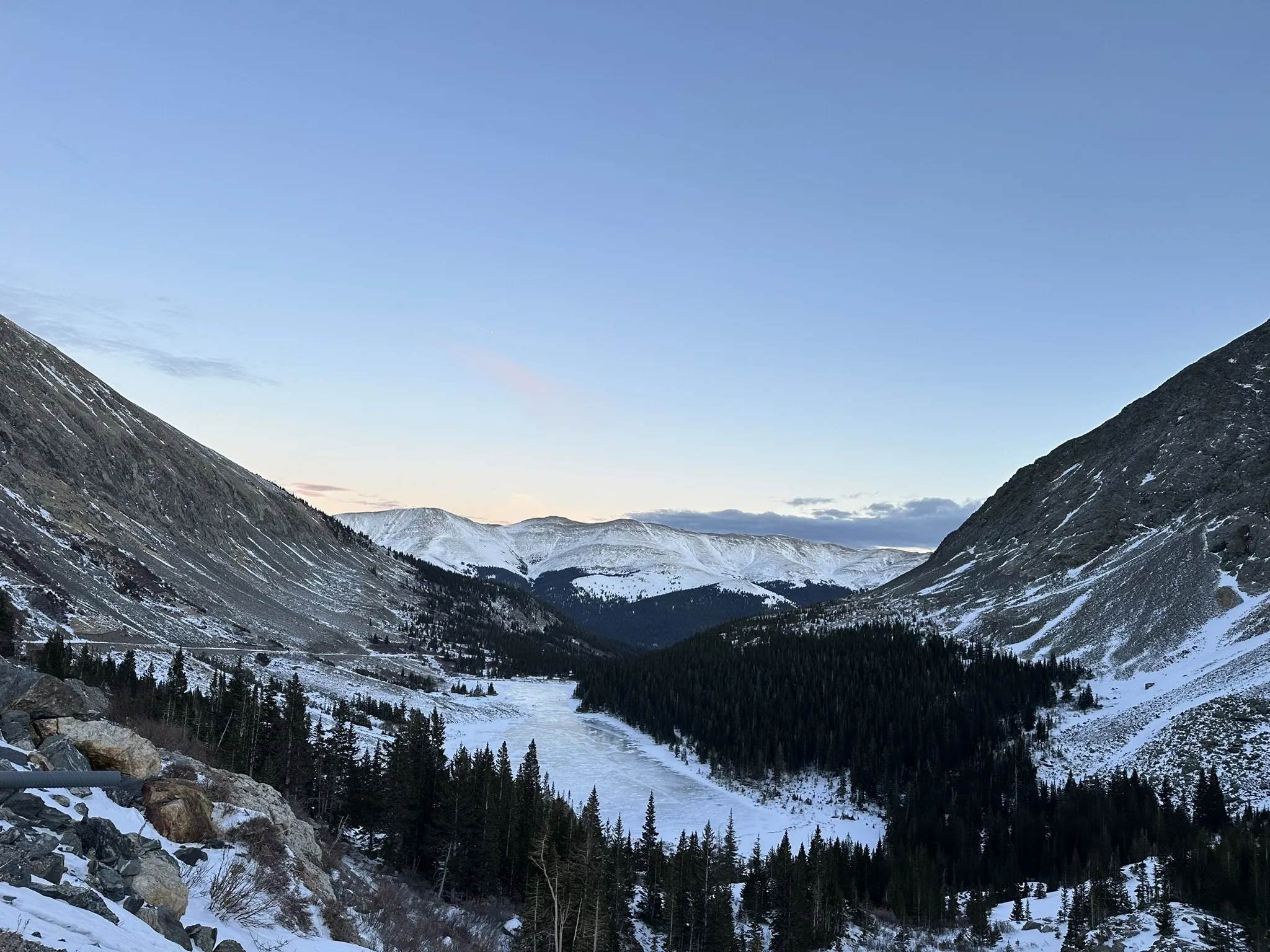 Lower Blue Lake at dusk, frozen in a wide alpine valley with spruce forest and snow-covered mountain ridges near Breckenridge, Colorado